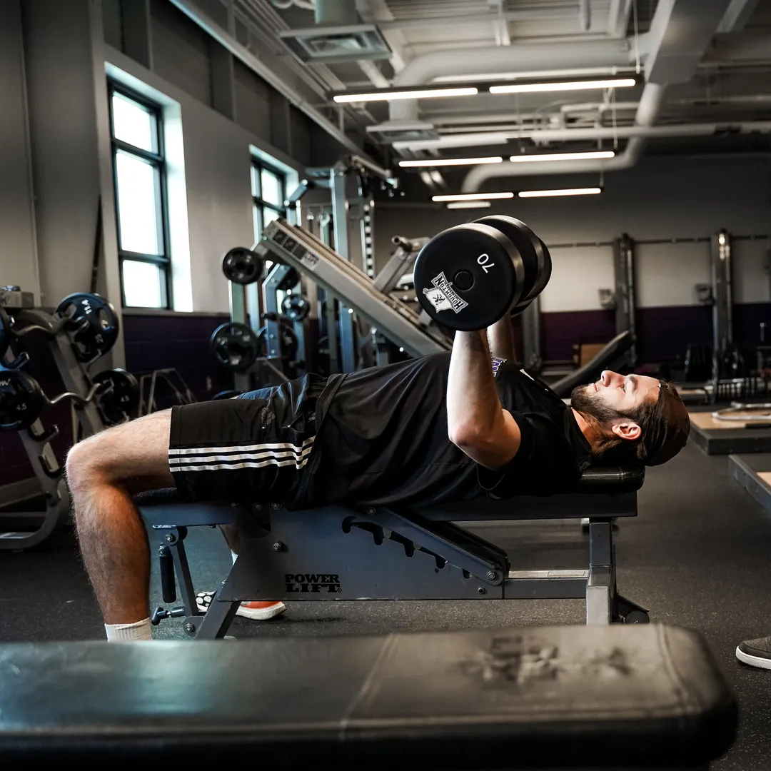 Houghton student athlete lifting weights in fitness center.