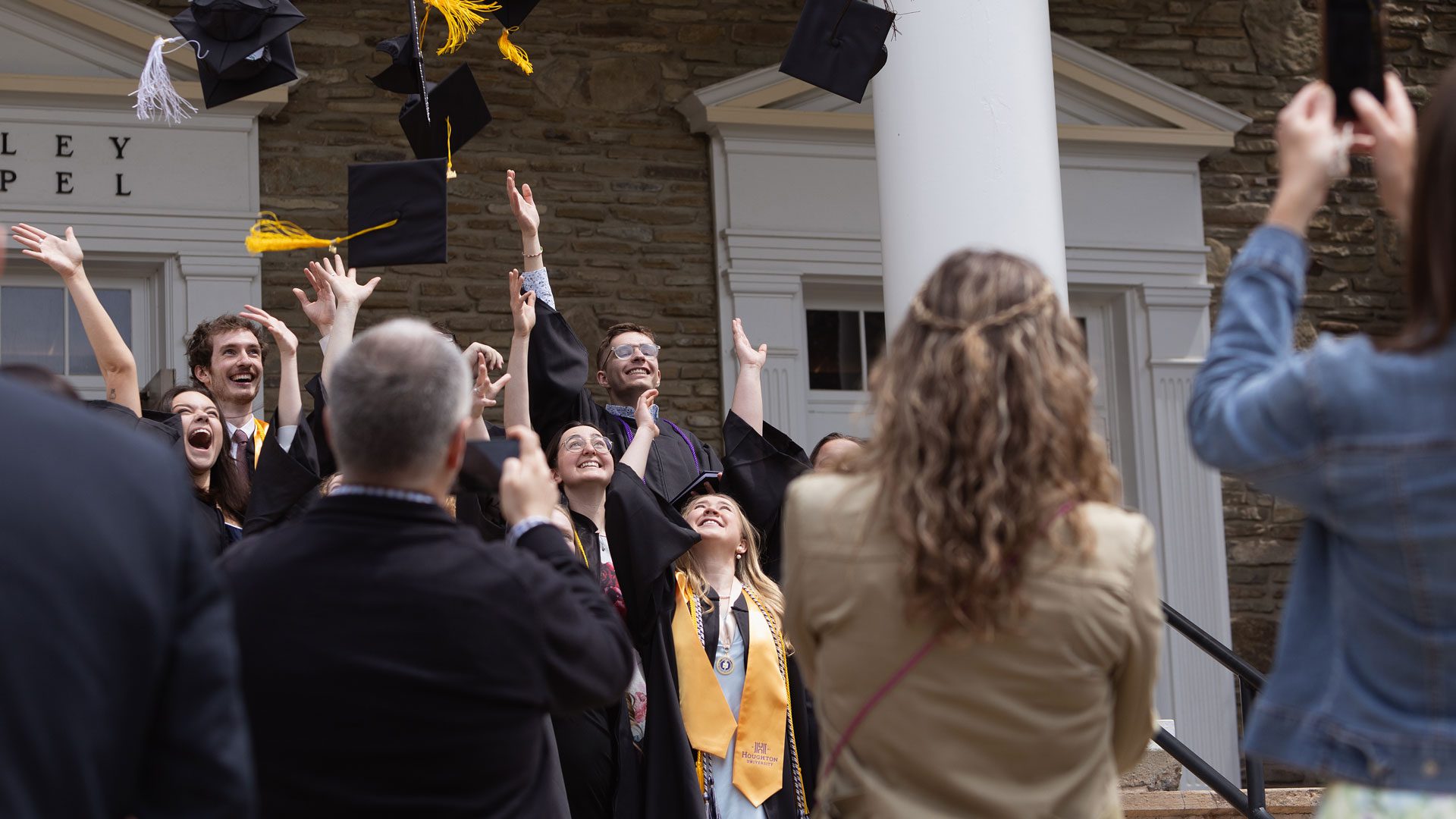 Graduates toss caps in the air in front of the chapel at commencement 2024