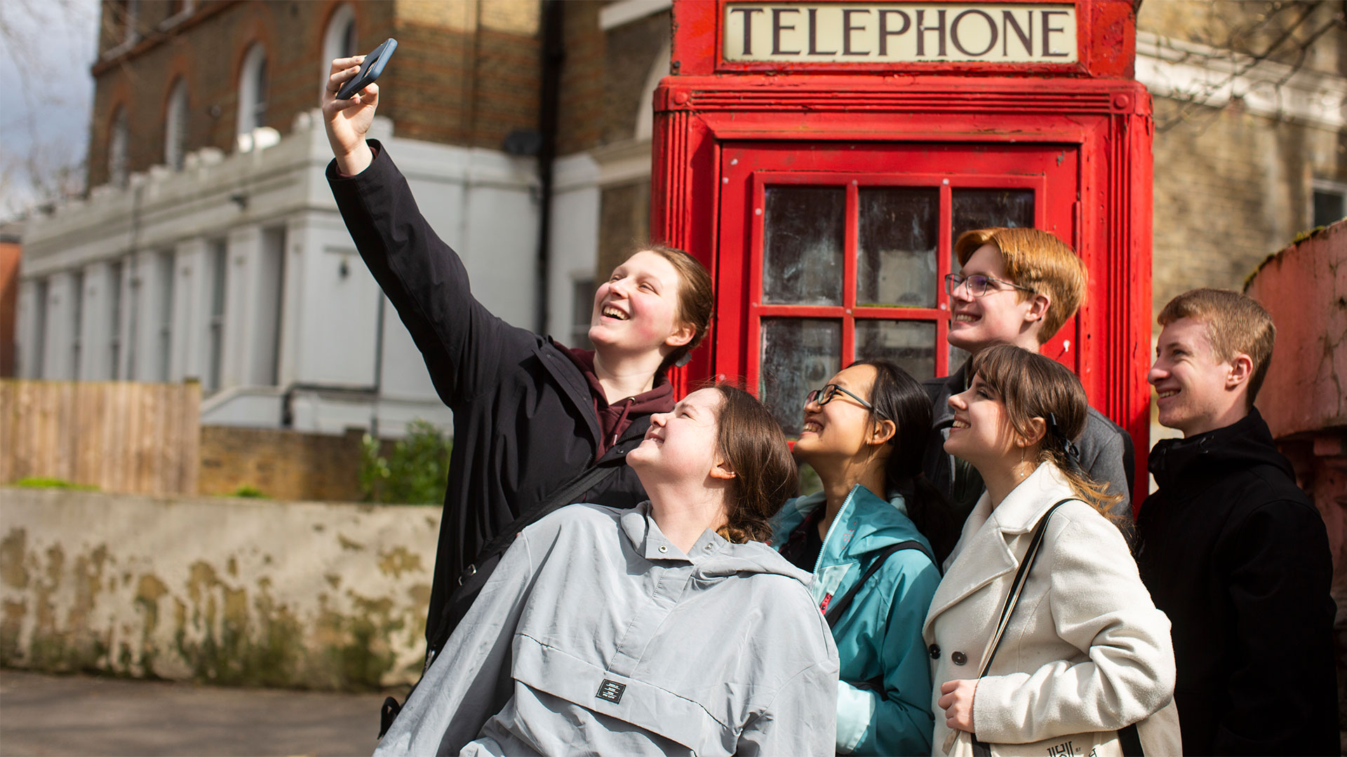 students smiling as they take a photo in front of a red London phone booth