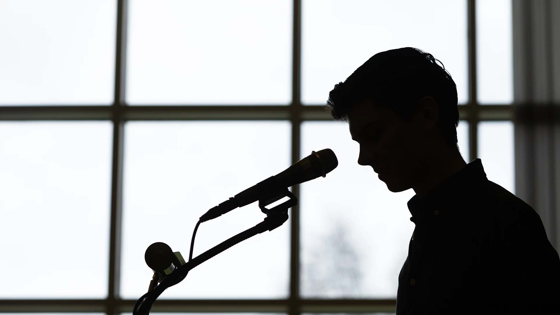 Recent Houghton alumnus Cody Johnson at podium with mike in silhouette.