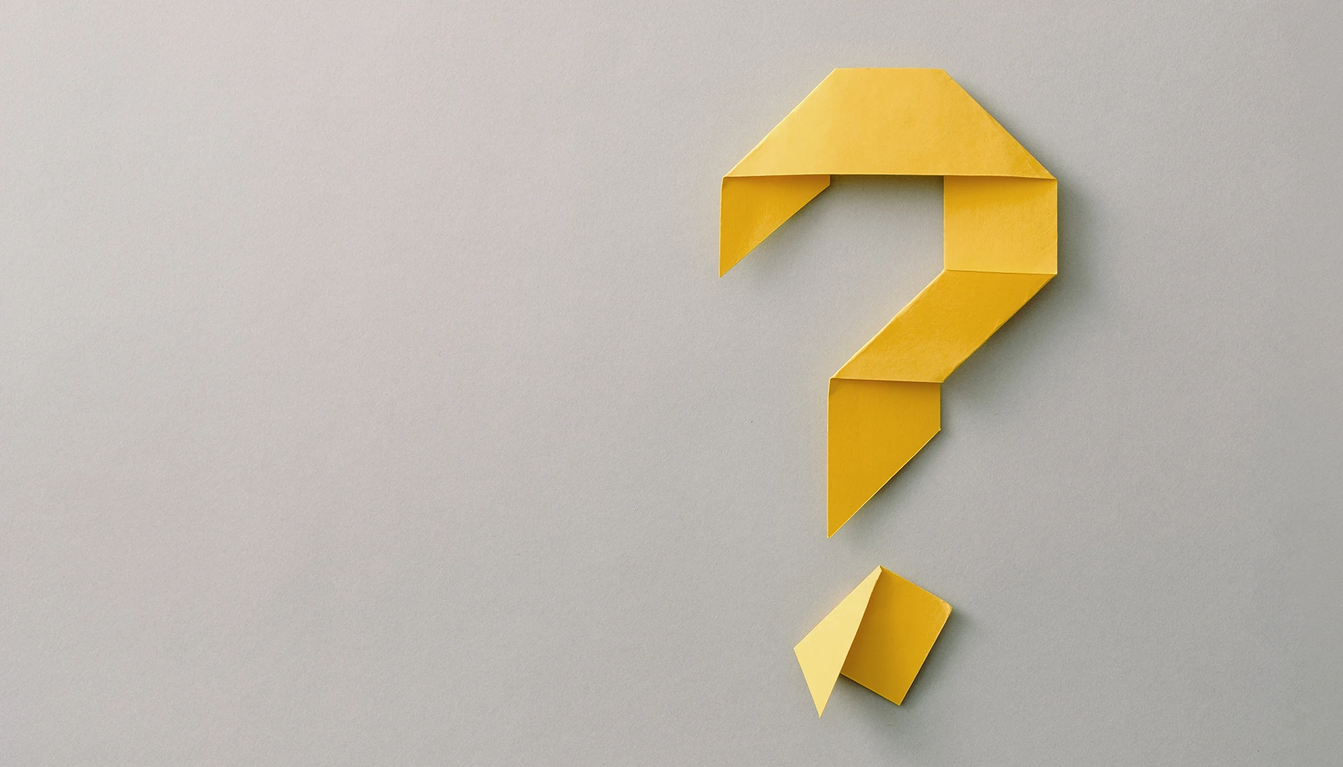 Yellow question mark made with origami paper on gray background.