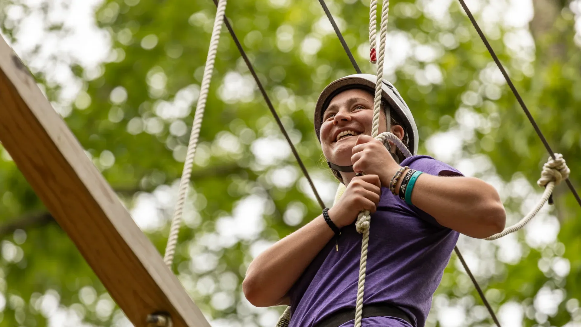 Houghton student standing on Epic Adventures ropes course wearing purple shirt and helmet.