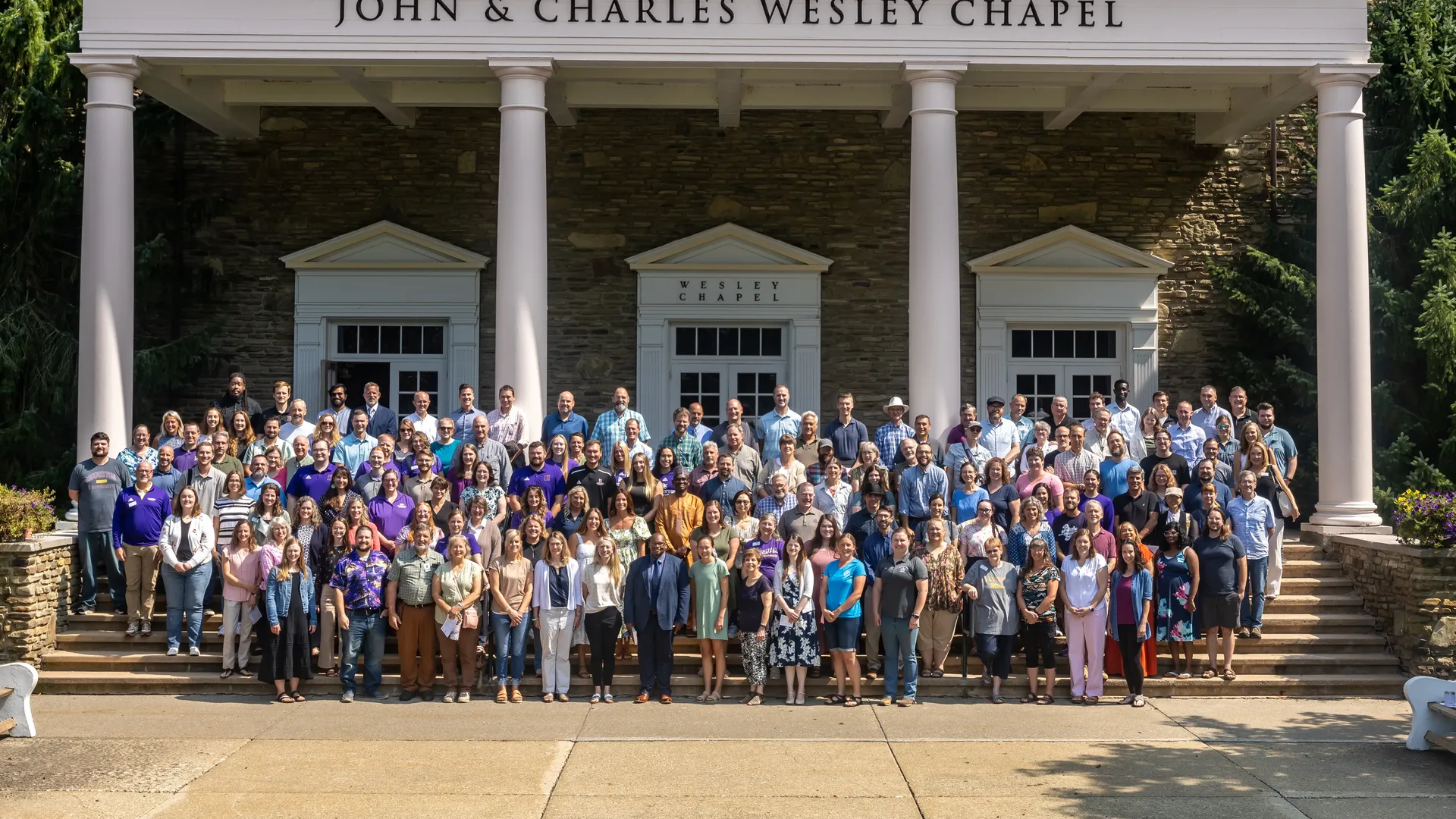 Houghton staff and faculty standing on the steps of the Wesley Chapel.