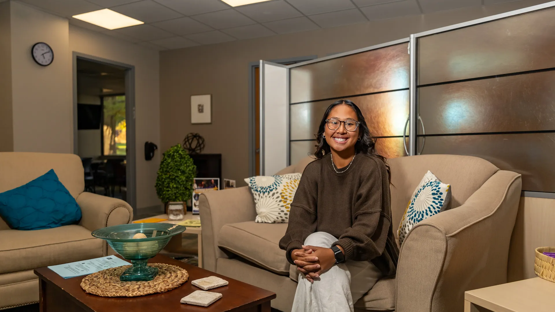 Houghton student MyaKay Bartman sitting on couch in campus office space.