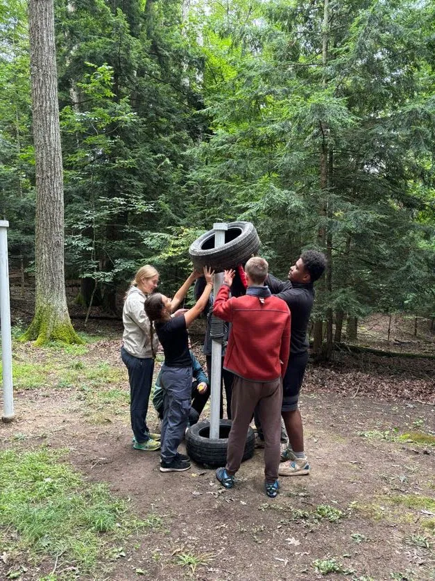 Houghton Highlander Wilderness Adventure students working on solving tire obstacle.