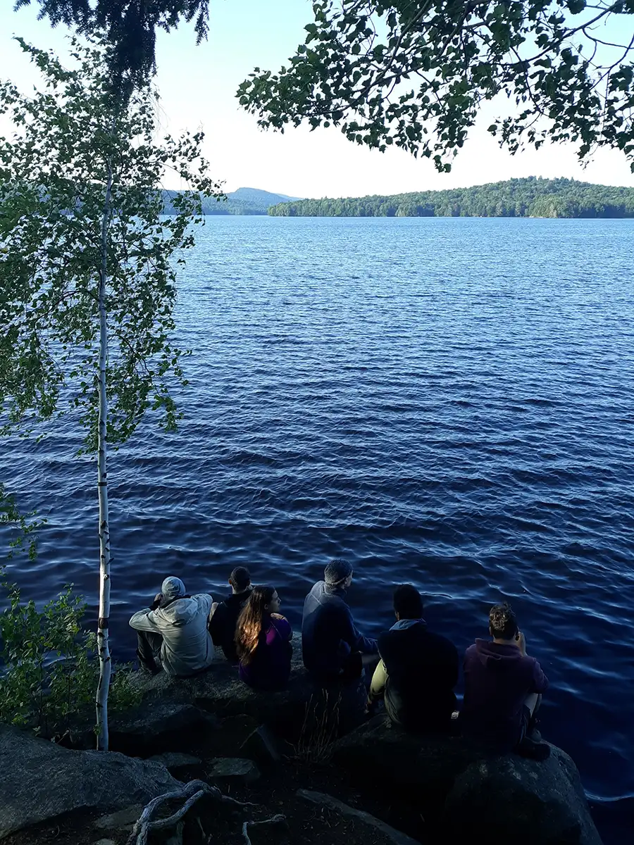 Group of Houghton Highlander Wilderness Adventure students sitting by shoreline.