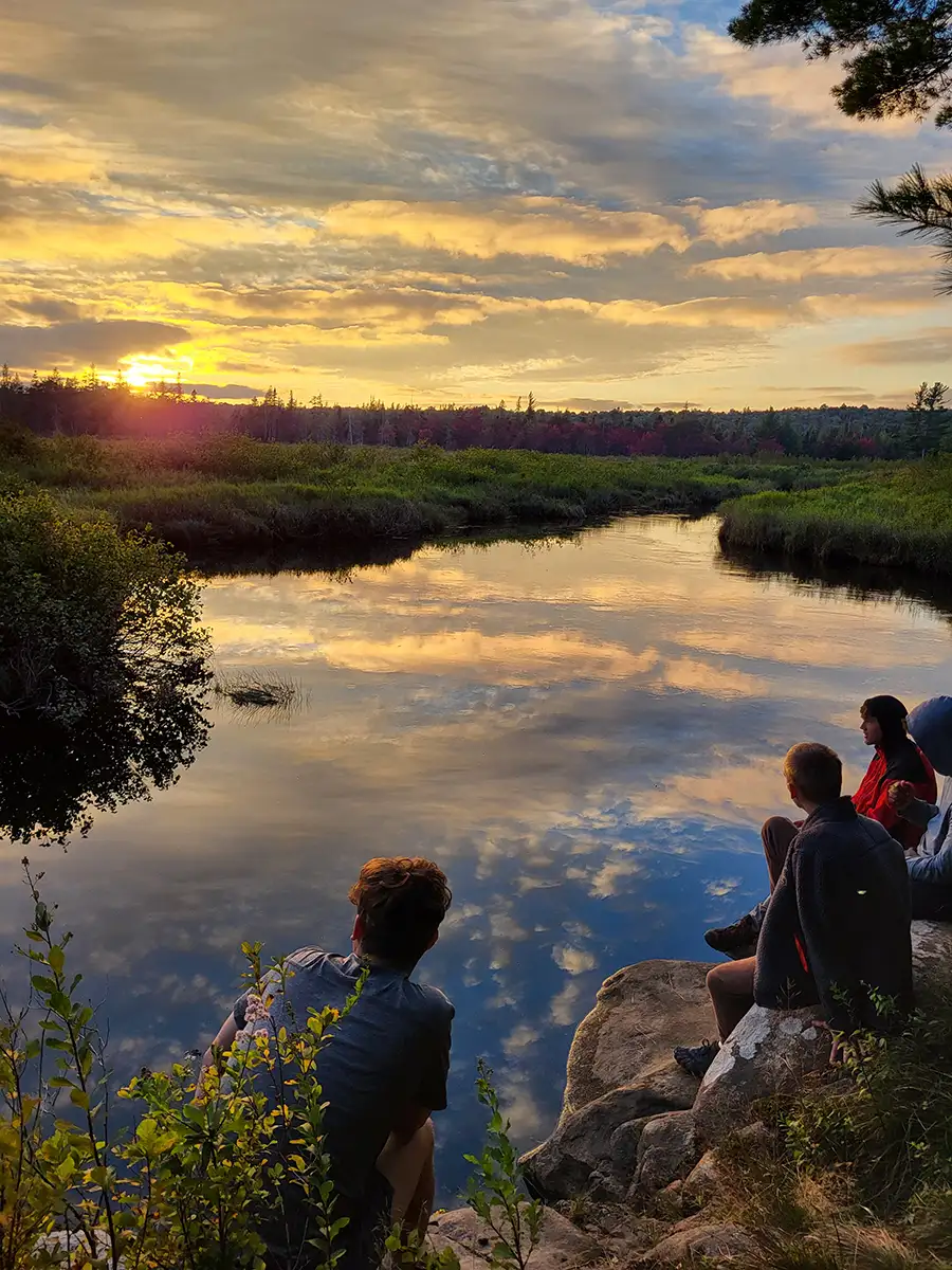 Houghton Highlander Wilderness Adventure students watching sunset over lake with reflection.