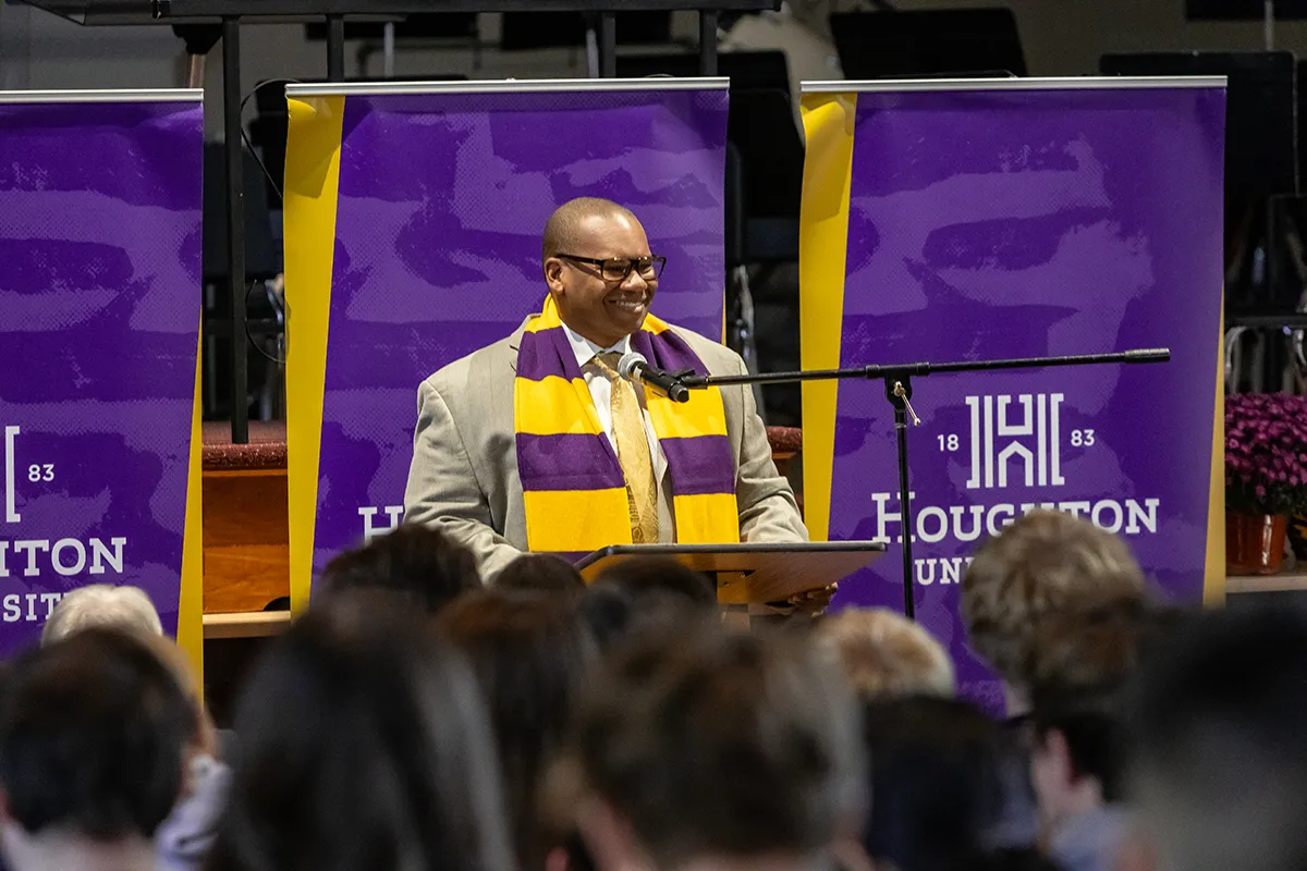 Houghton University president Wayne Lewis standing at podium wearing purple and gold scarf.
